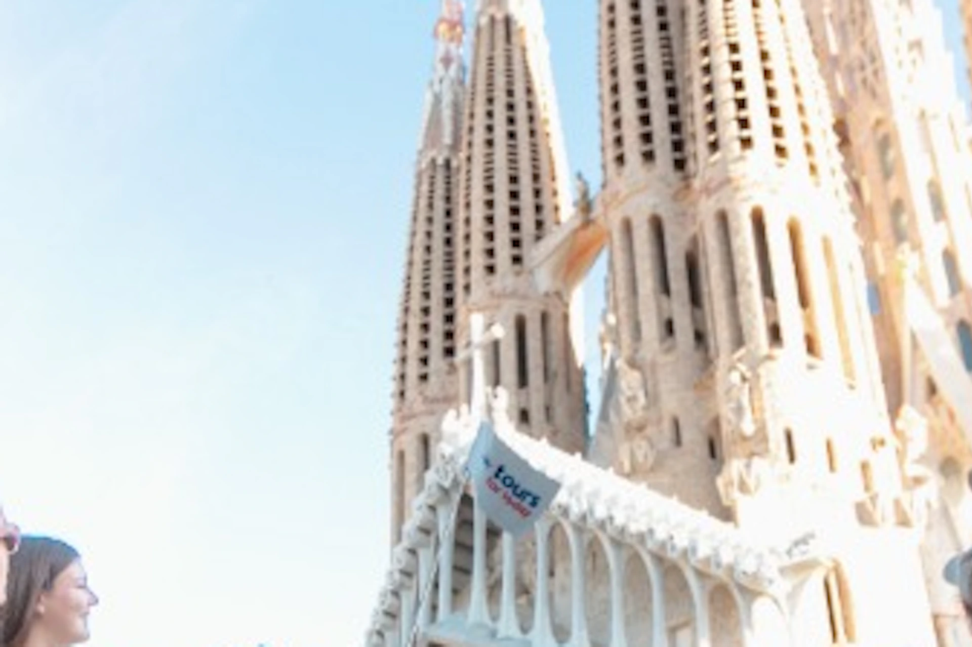 A group of people standing outdoors, looking at the Sagrada Familia basilica under a clear blue sky.