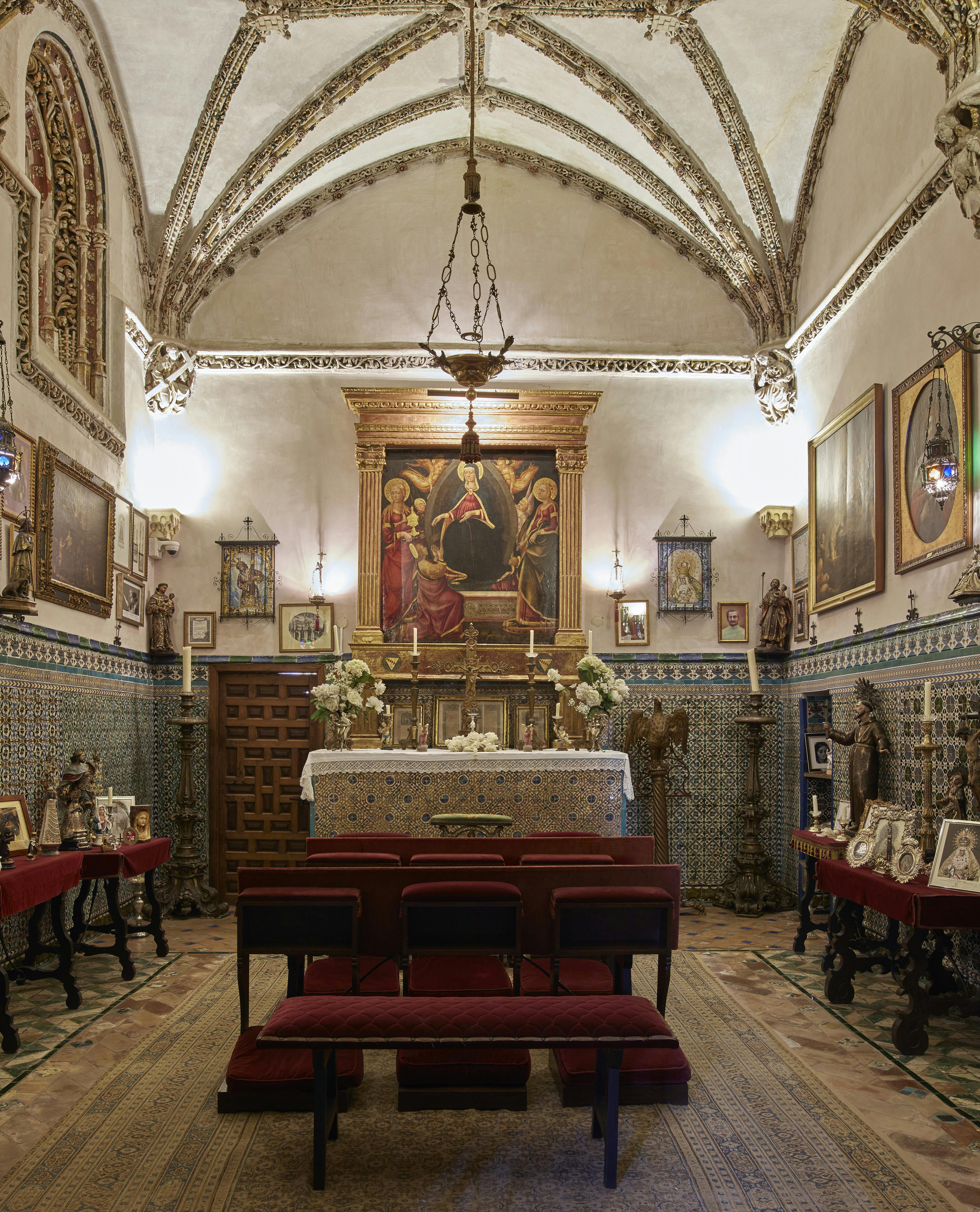 Small chapel with an ornate altar, religious paintings, and six red chairs. Chandeliers hang from the arched ceiling.