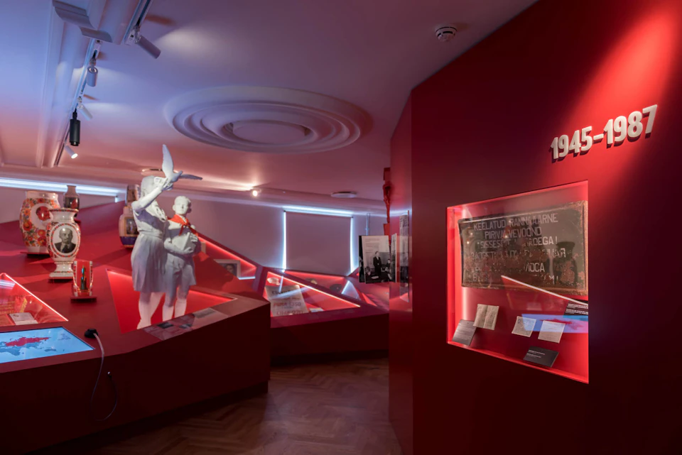 A museum exhibit room with red walls, mannequins in period clothing, and illuminated display cases.