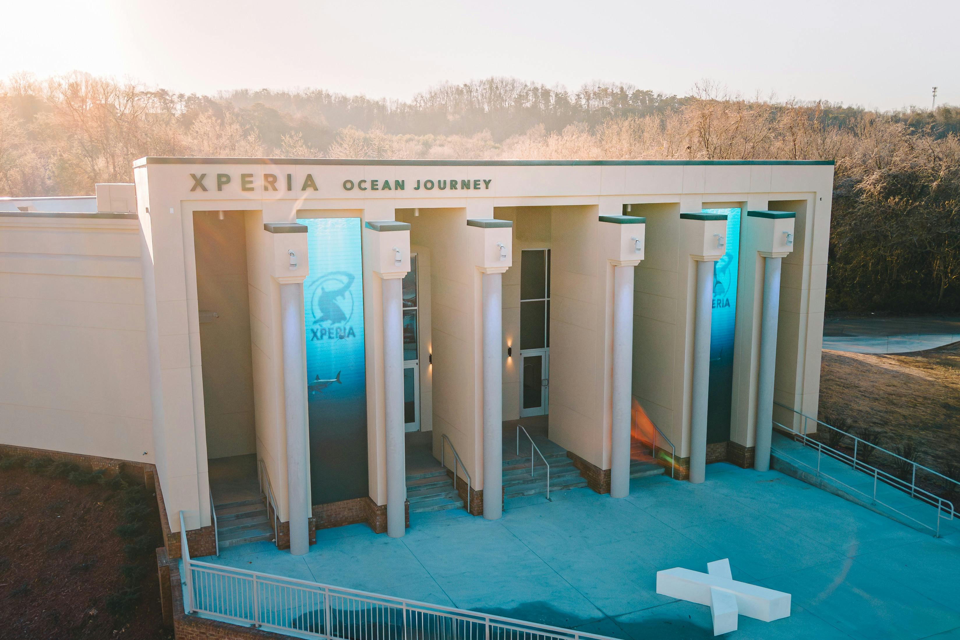 Entrada a un edifici anomenat "Xperia Ocean Journey" amb grans columnes, pantalles digitals blaves i escales que condueixen a les portes.