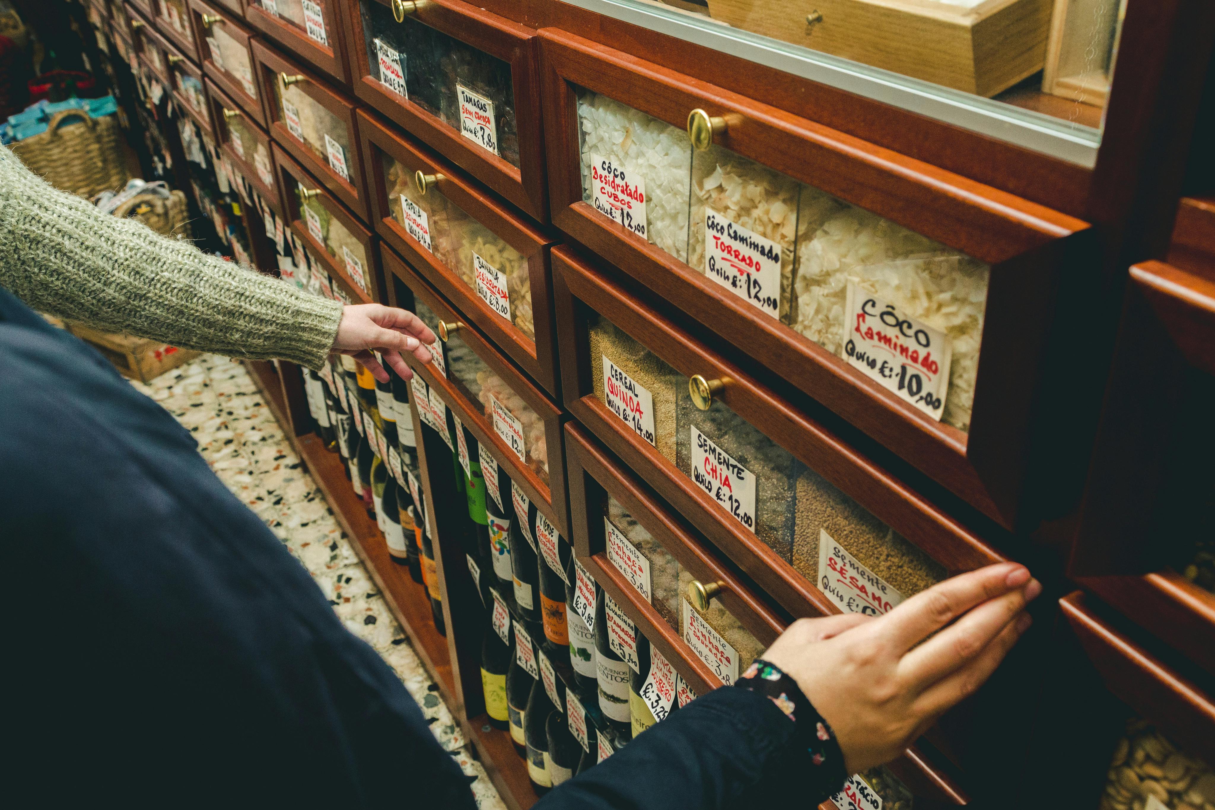 Οι άνθρωποι περιηγούνται σε συρτάρια με ετικέτες γεμάτα με διάφορους κόκκους και ράφια εφοδιασμένα με μπουκάλια σε ένα κατάστημα.