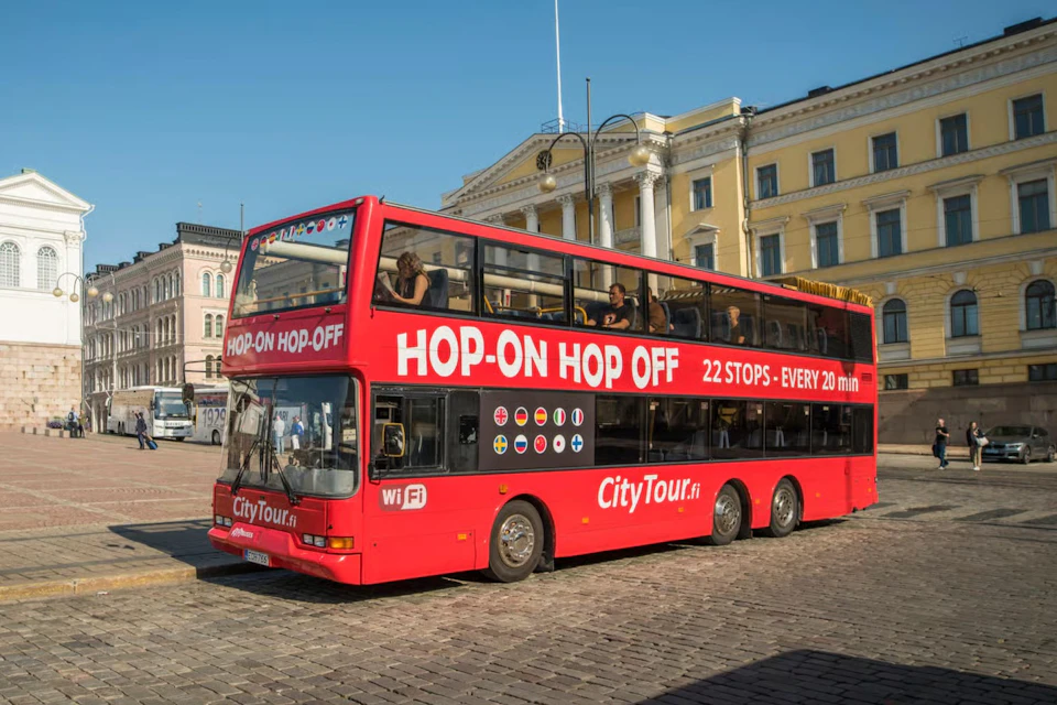 A red double-decker bus labeled "Hop-On Hop-Off" parked on a cobblestone street with a historic building in the background.