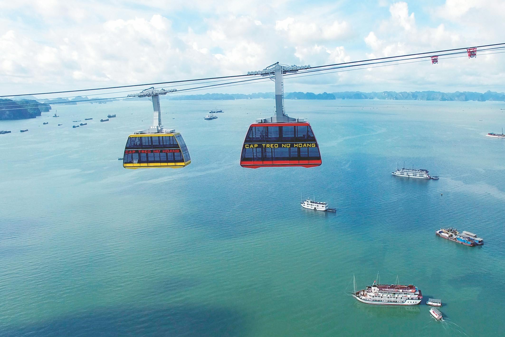 Two gondola cable cars suspended over a large body of water, with boats and distant land visible in the background.
