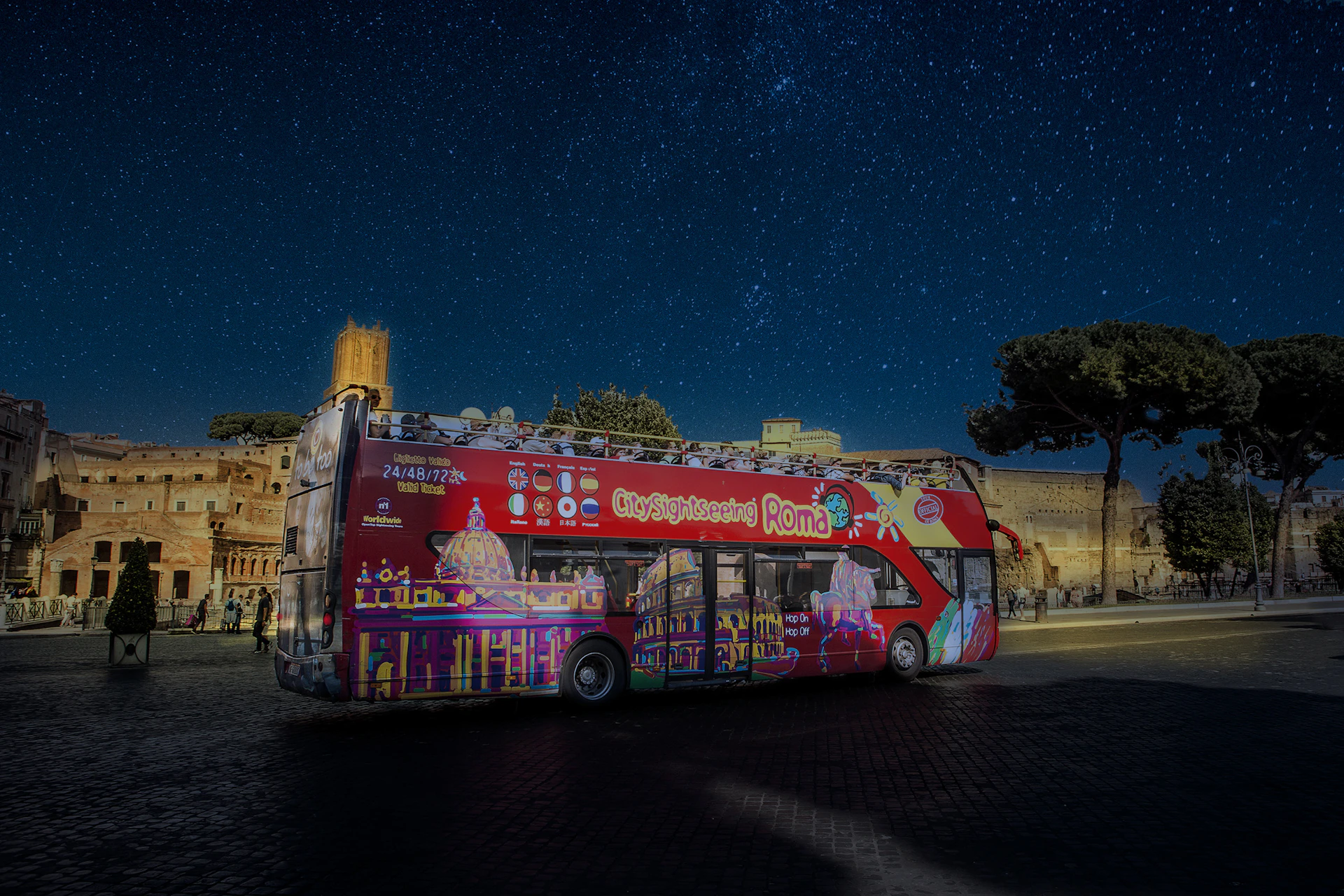 A red double-decker sightseeing bus in Rome at night with a starry sky and historic buildings in the background.