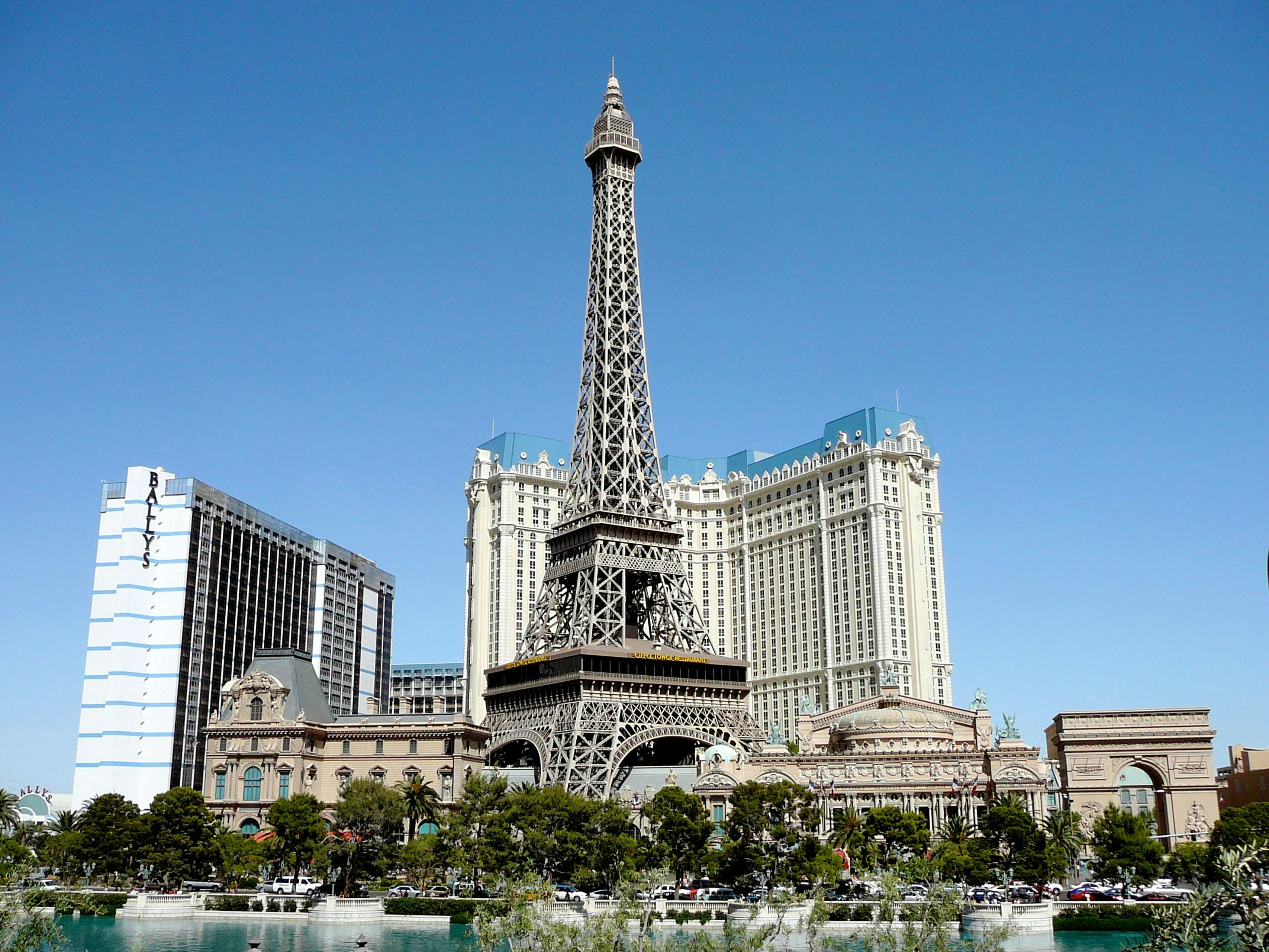 A replica of the Eiffel Tower stands among tall buildings and greenery under a clear blue sky.