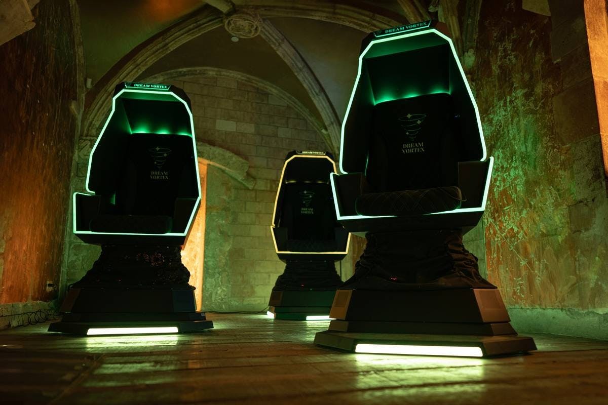 Tre sedie nere futuristiche con bordi verdi luminosi in una stanza poco illuminata con pareti e archi in pietra.