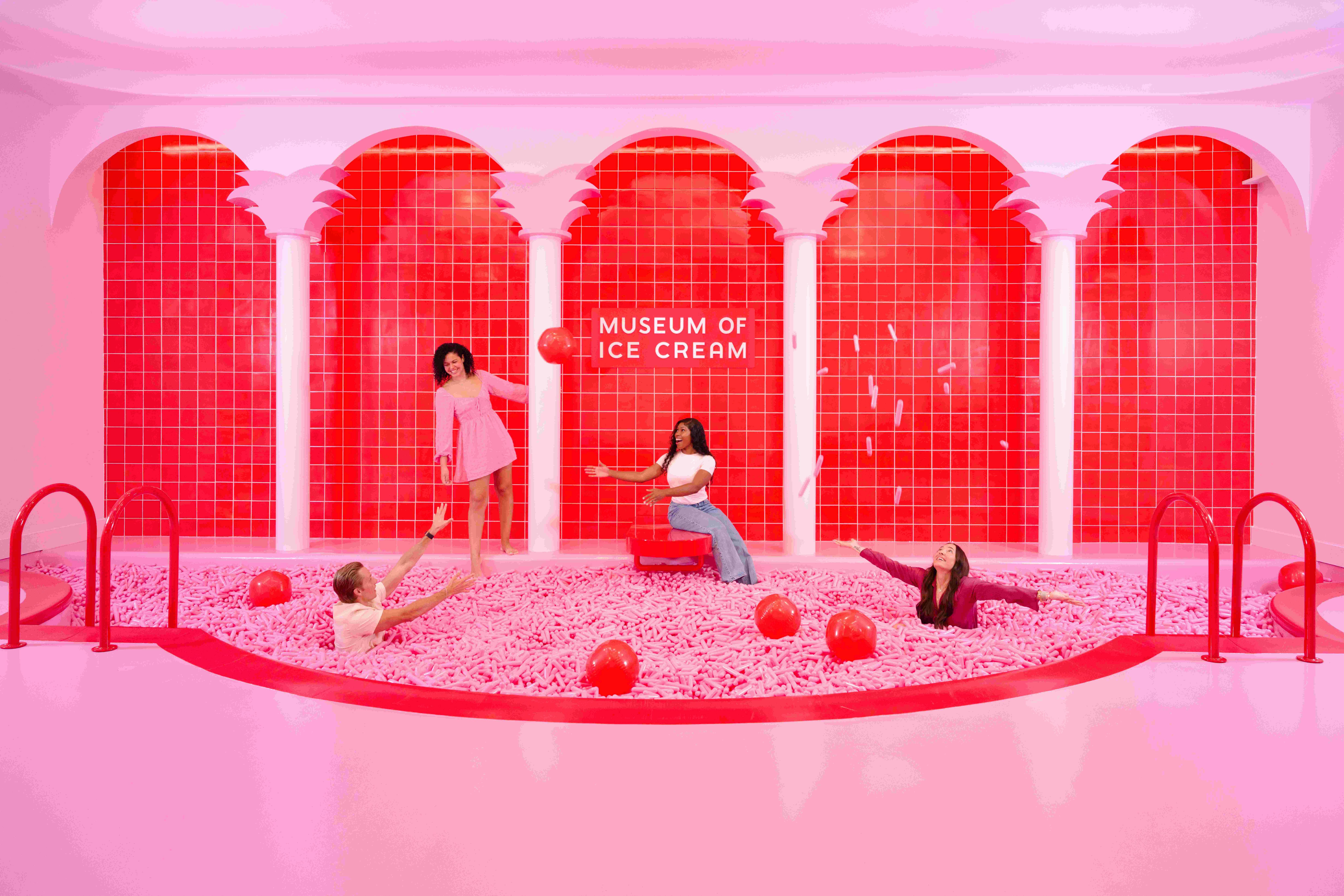4명은 '아이스크림 박물관' 이라는 이름의 아치형 통로 아래 분홍색 볼 구덩이에서 빨간 공을 들고 포즈를 취하고 놀고 있습니다.