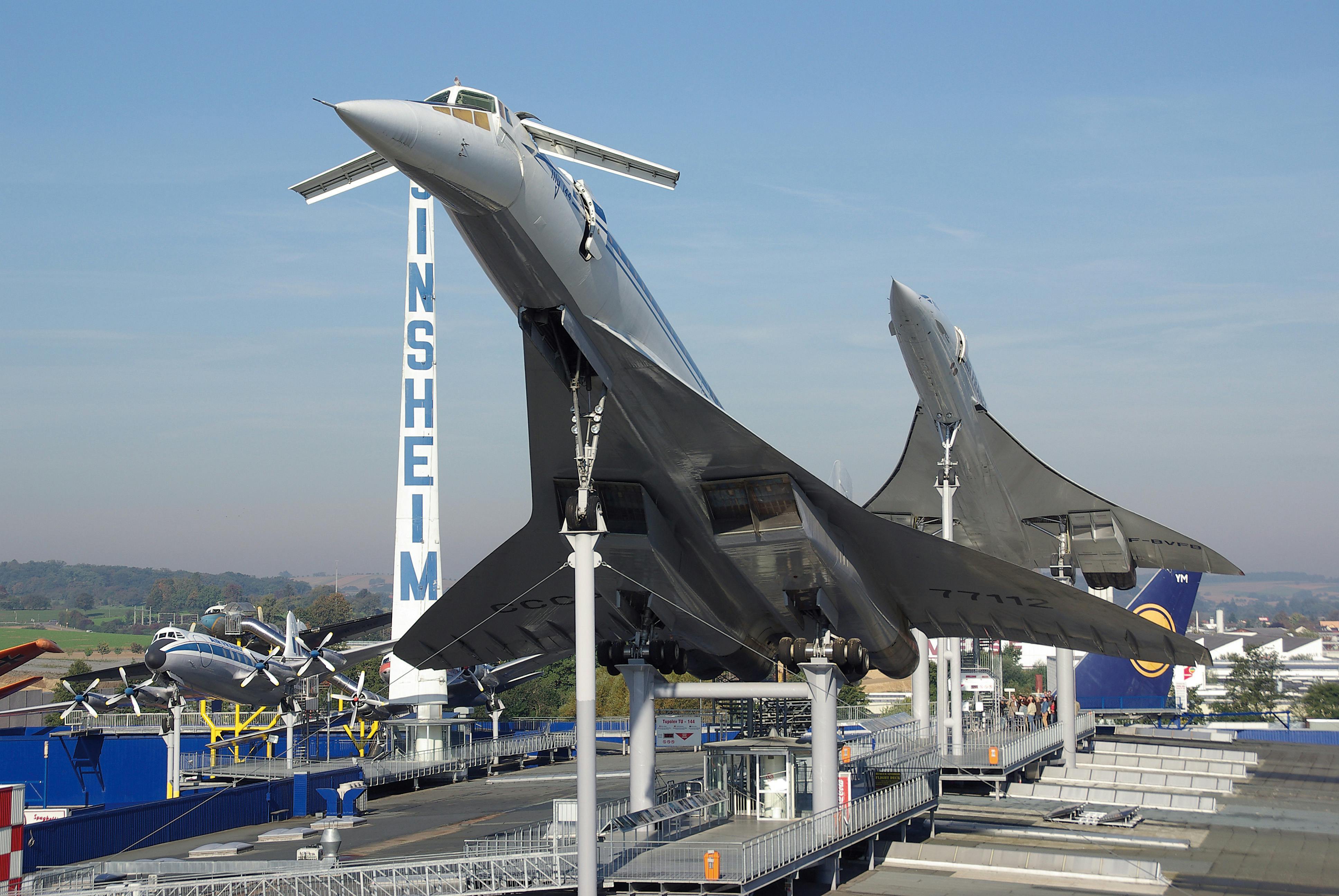 Två Concorde-flygplan visas på upphöjda plattformar på ett utomhusmuseum, med flera andra flygplan synliga i bakgrunden.