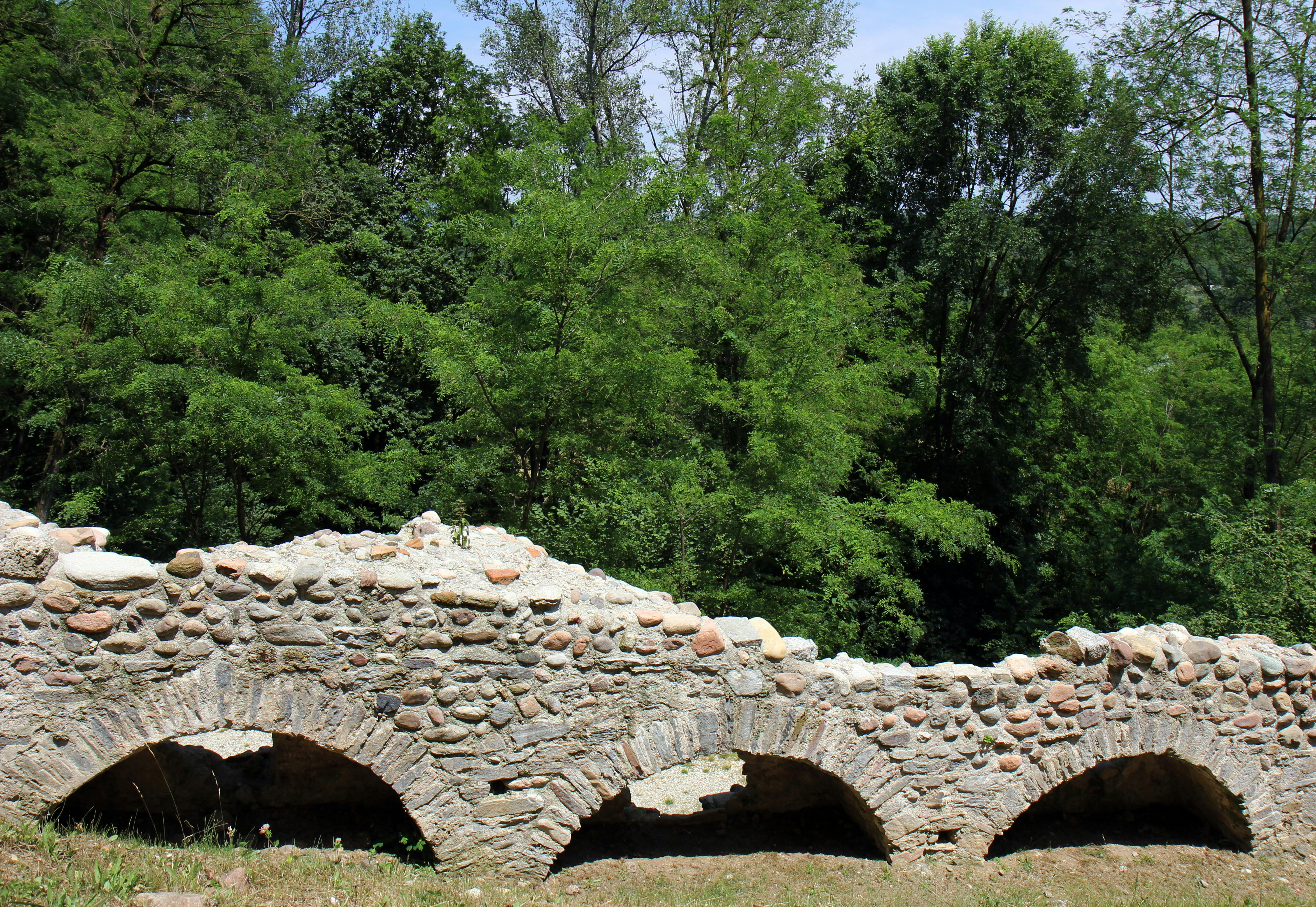 Ancient stone aqueduct with multiple arches surrounded by green trees and foliage.