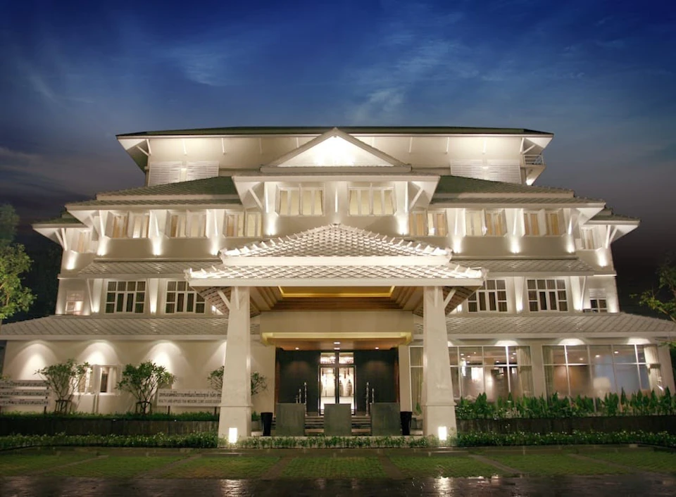 A well-lit building at night featuring a symmetrical facade, large entryway with pillars, and landscaping in front.