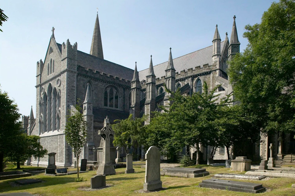 A historic stone cathedral with pointed arches and tall spires, surrounded by grassy grounds and old tombstones.
