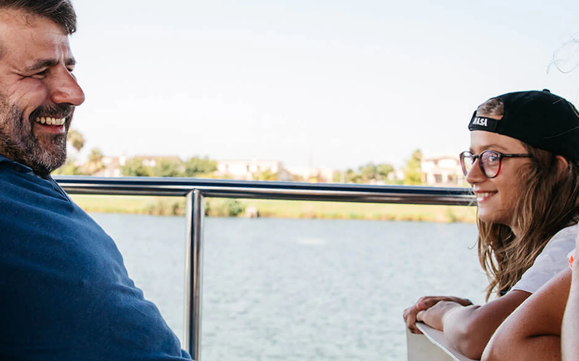 Four people smiling and laughing on a boat ride, with water and greenery in the background.