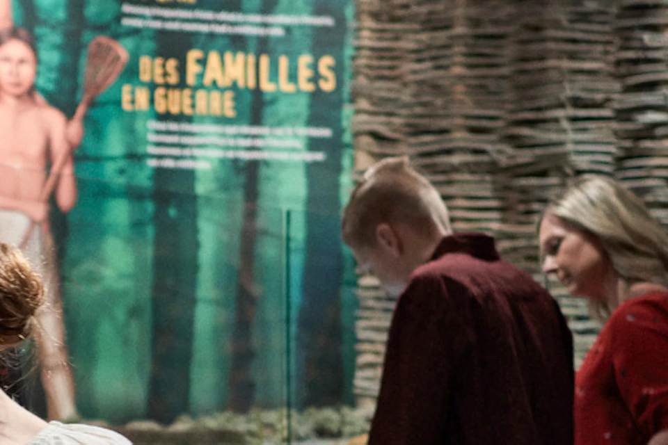 A woman and a child engage with a prehistoric exhibit in a museum. Other visitors are viewing displays in the background.
