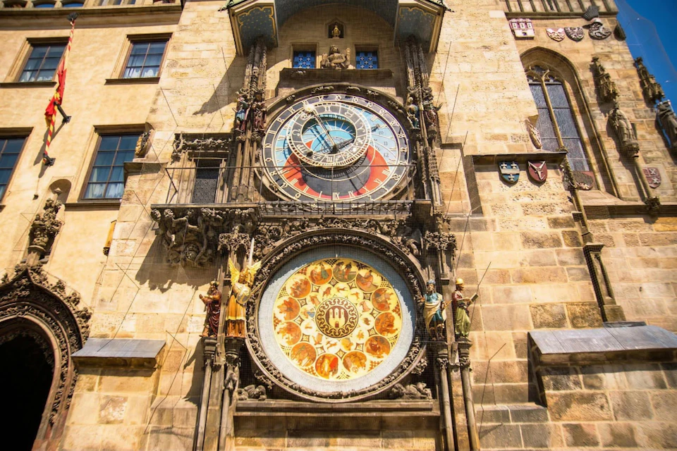 A detailed astronomical clock on a historic building facade, featuring intricate dials and decorative statues.
