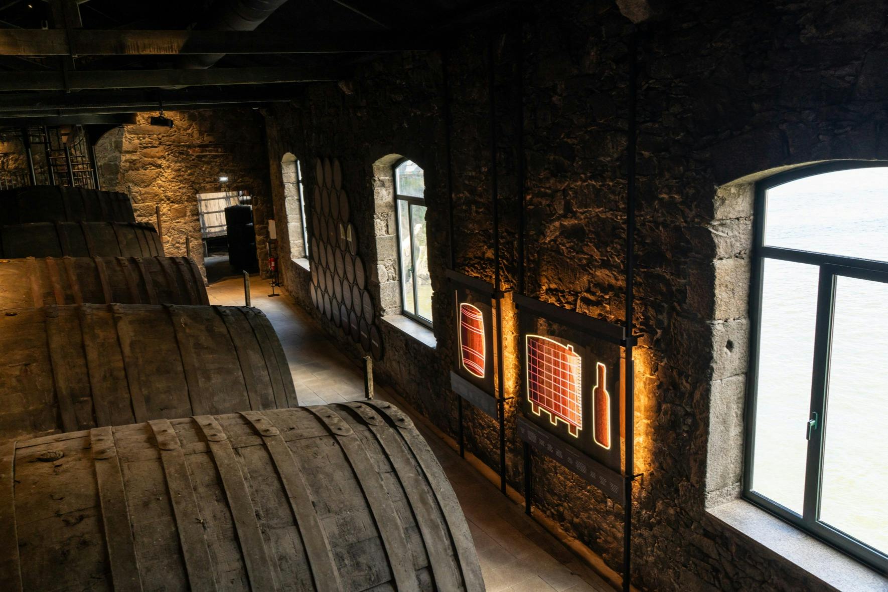 Intérieur d'une cave rustique avec de grands tonneaux en bois et des diagrammes éclairés de la production de vin sur le mur de pierre.