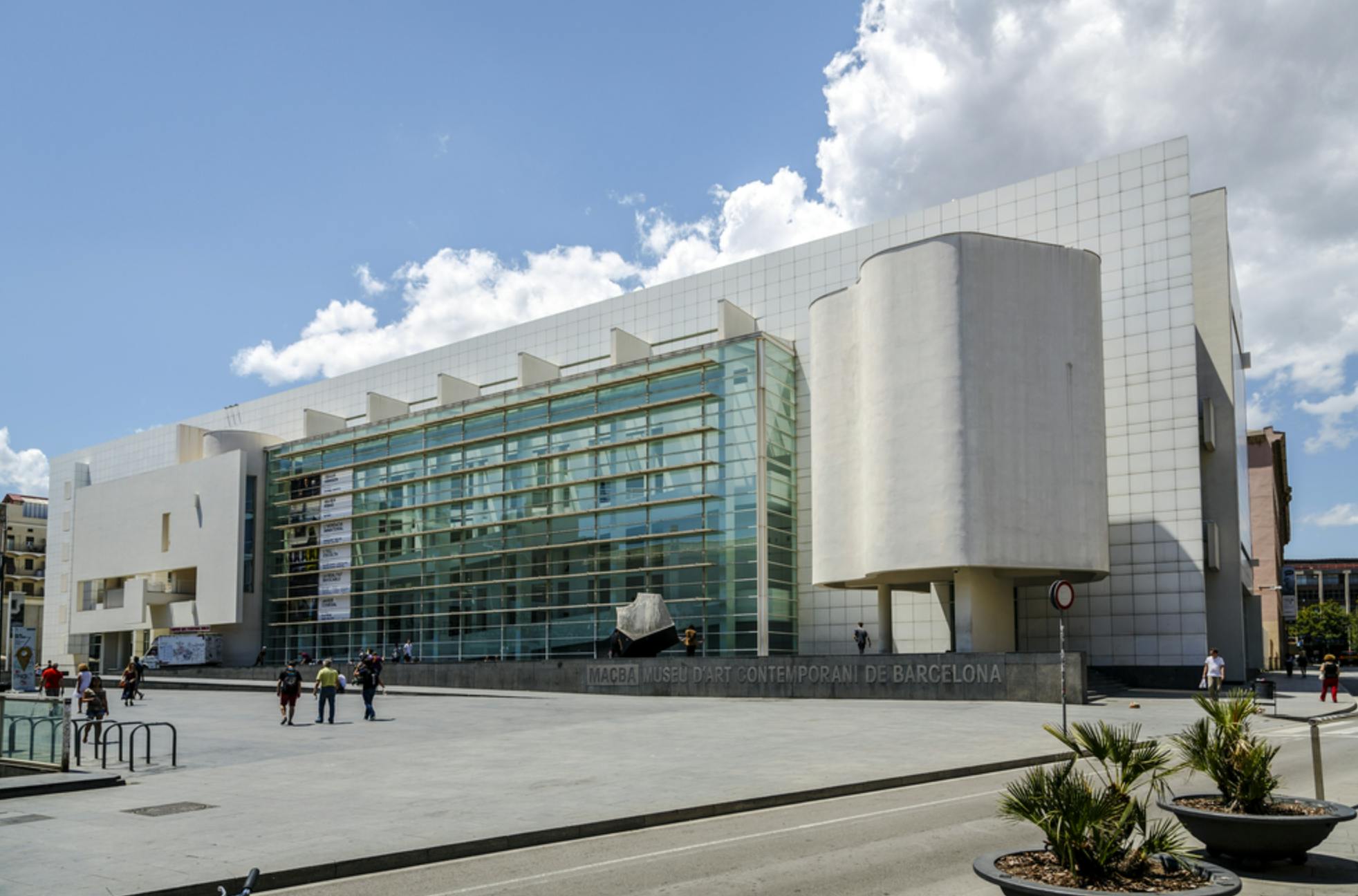 En modern byggnad med glas och vita väggar, märkt MACBA Museu d'Art Contemporani de Barcelona, under en solig himmel.
