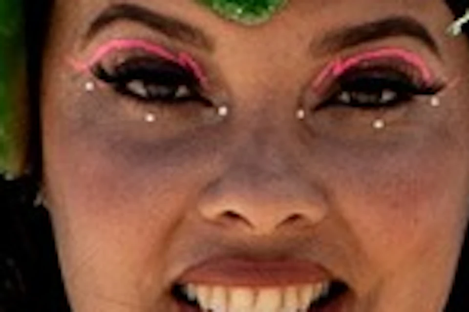 A person in an elaborate green costume poses on a sandy beach with the ocean in the background under a sunny sky.