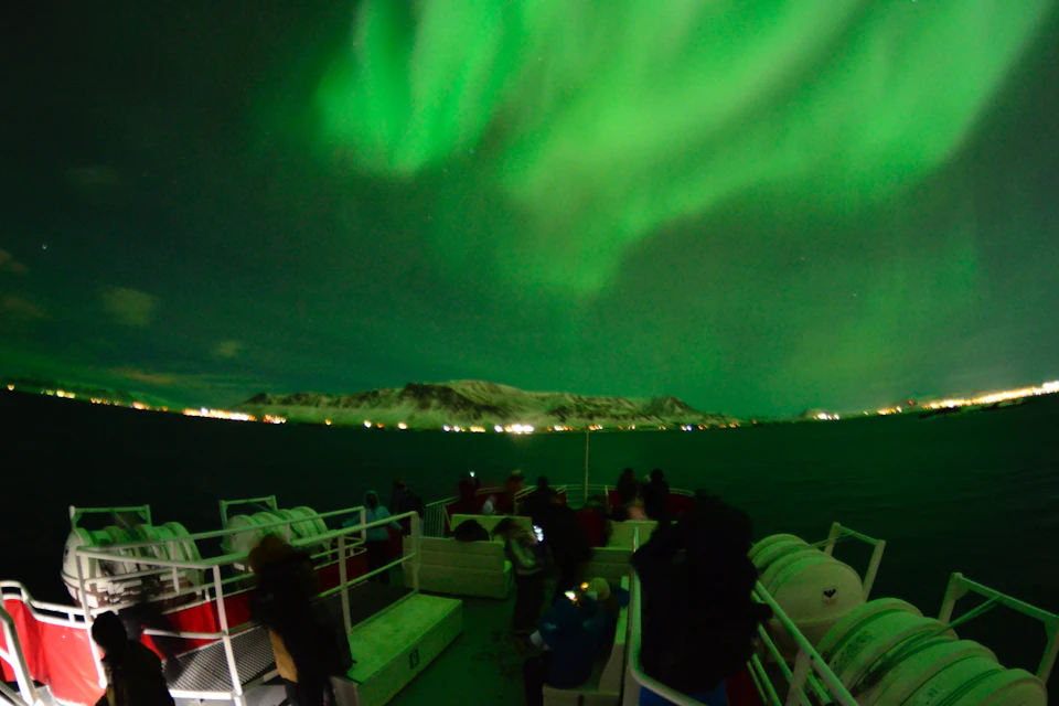Northern Lights light up the night sky and the boat with a green glow.