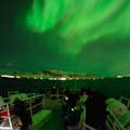 Nordlichter erhellen den Nachthimmel und das Boot mit einem grünen Schein.