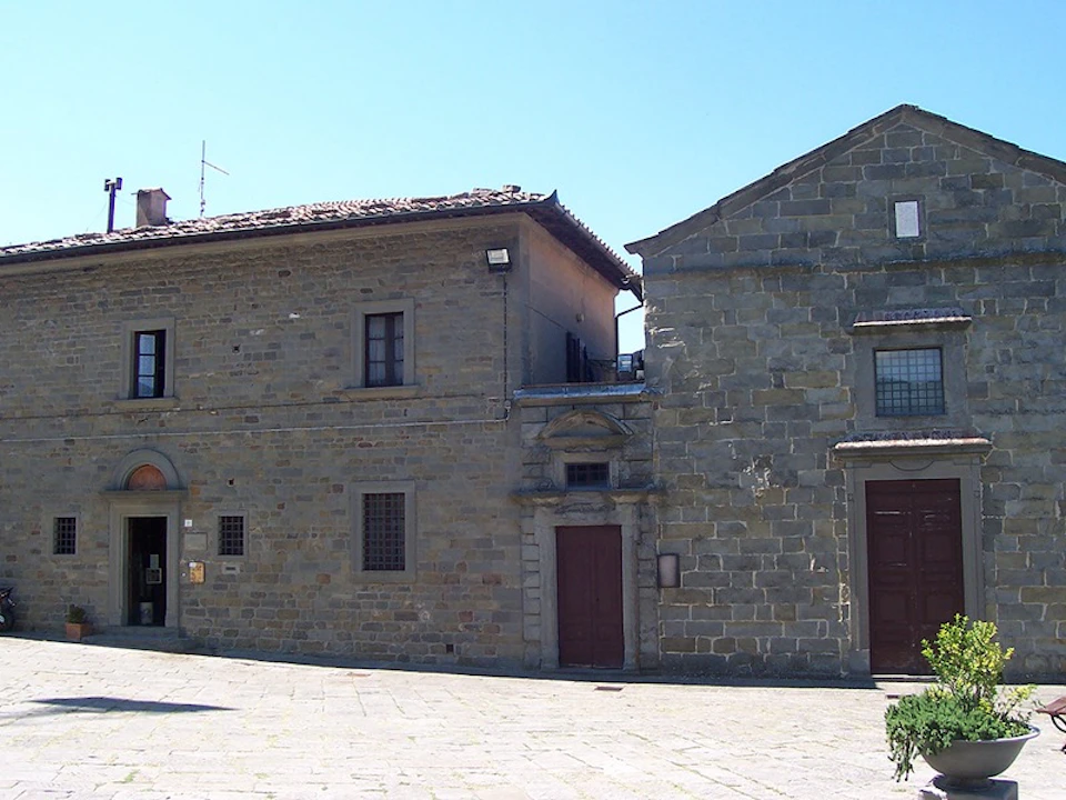 Two adjacent stone buildings with tiled roofs and shuttered windows under a clear blue sky.