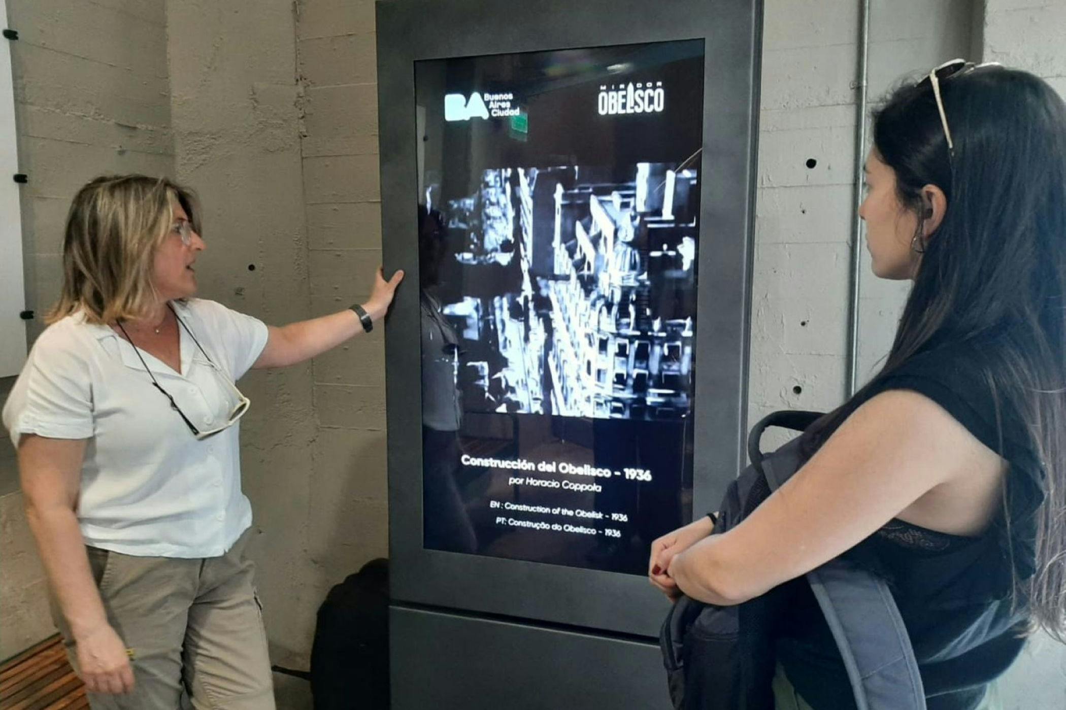 A woman standing next to a digital display showing historical information about the construction of the Obelisco in 1936.