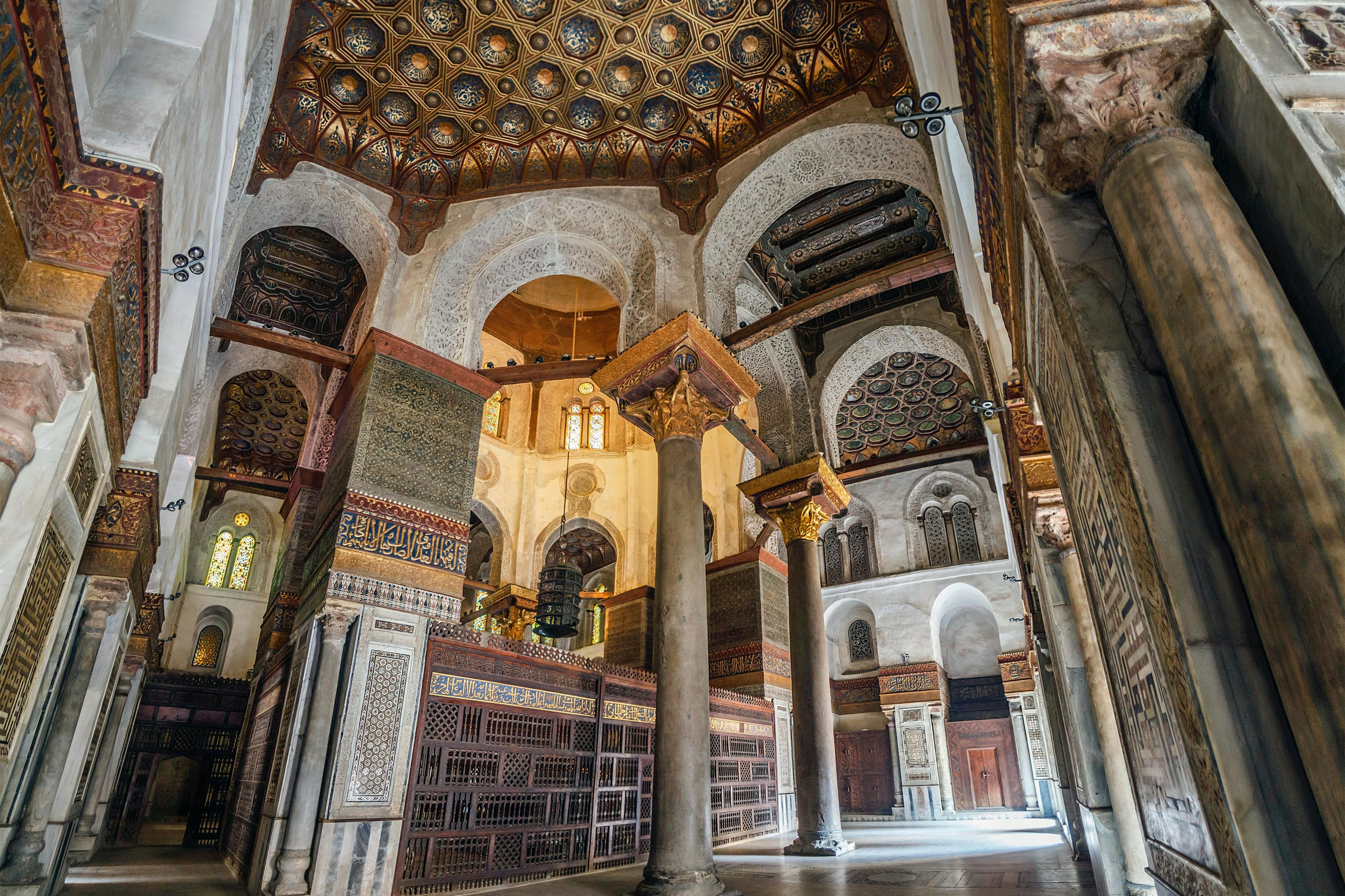 Сложный интерьер исторического здания с декоративными потолками, колоннами, арочными проемами и детальными узорами стен.