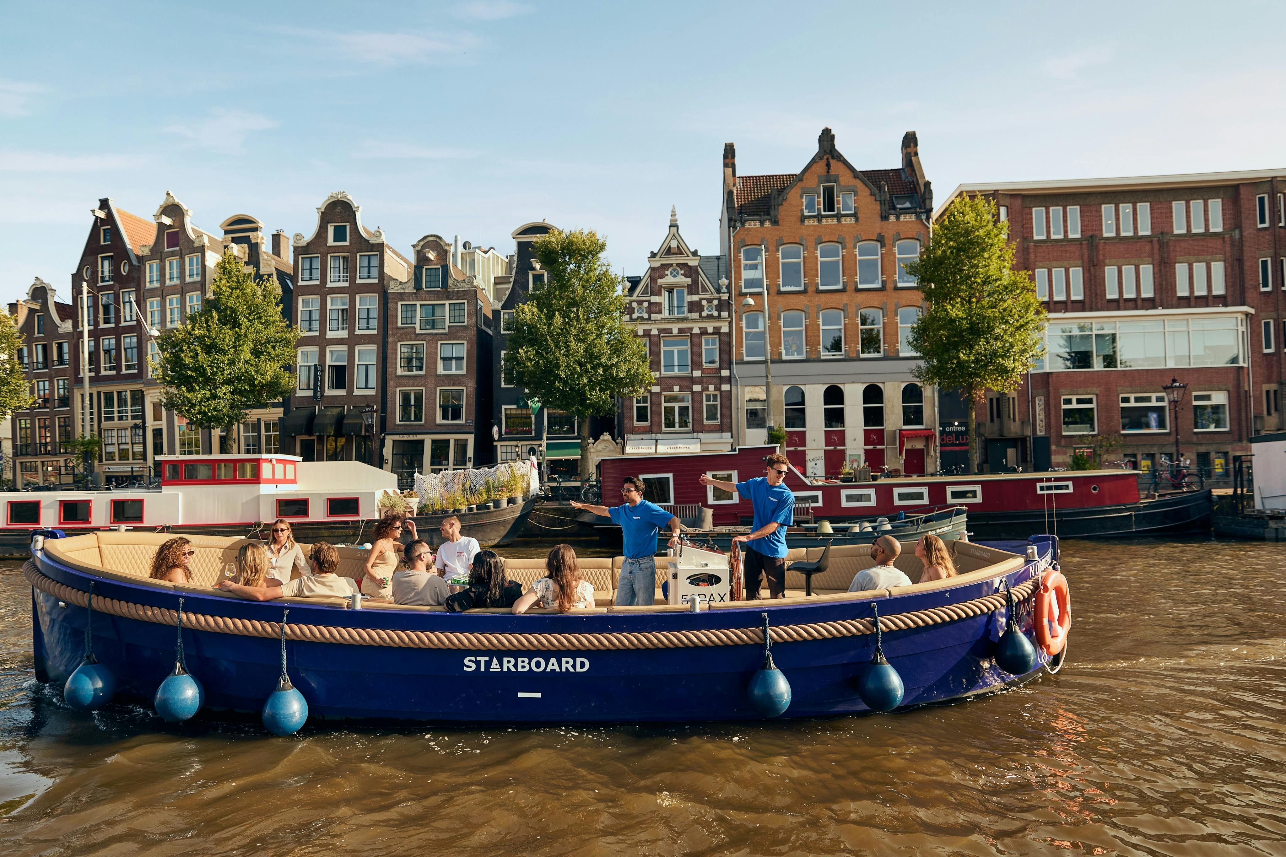 乗客と乗組員を乗せた「右舷」と呼ばれる運河ボートが、オランダの伝統的な建物の前の水路に沿って浮かんでいます。