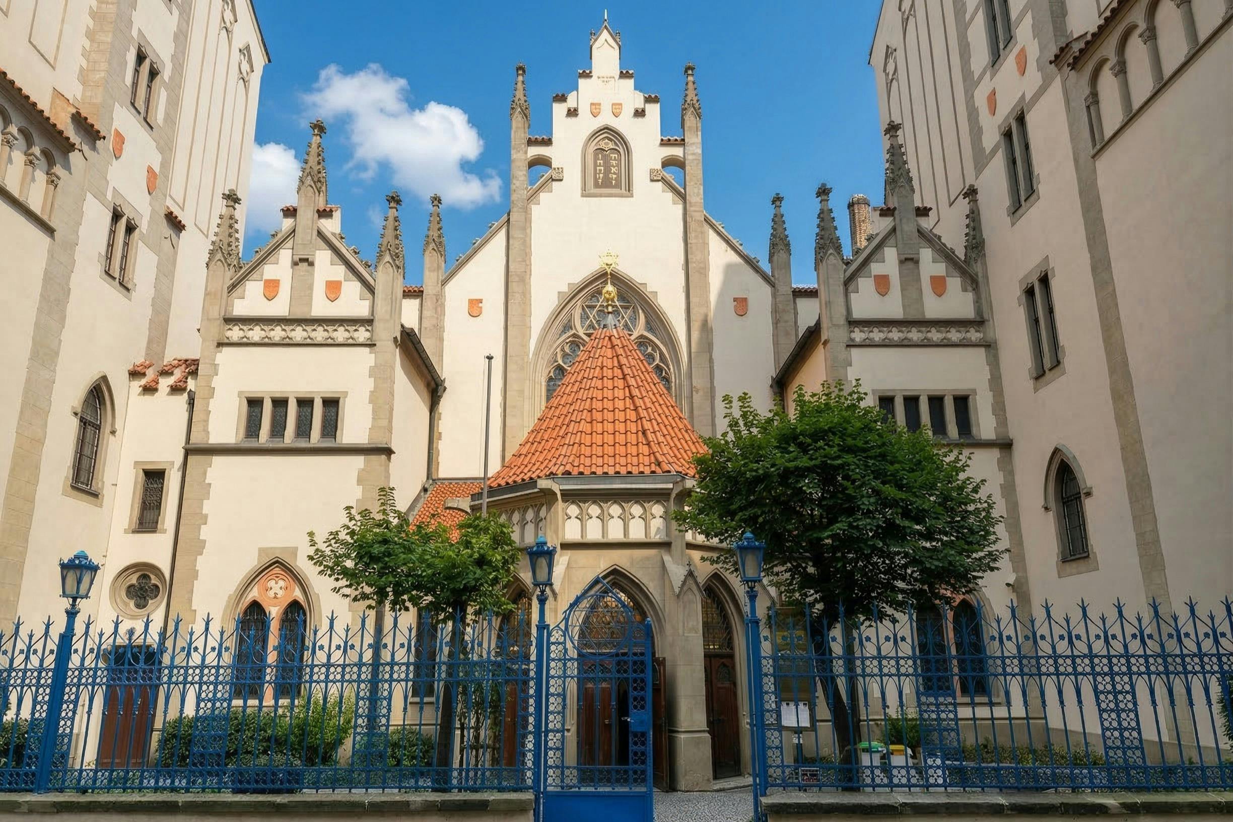 A historic building with pointed arches, ornate details, and a blue wrought iron gate under a clear sky.