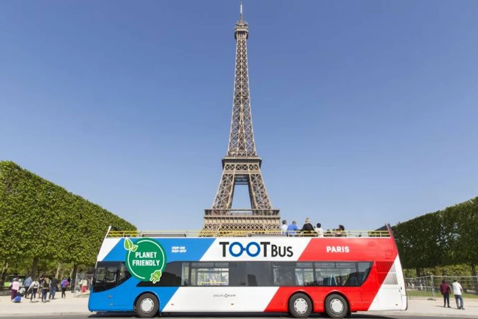 A double-decker tour bus with 'Planet Friendly' and 'TOOTBus Paris' branding in front of the Eiffel Tower.