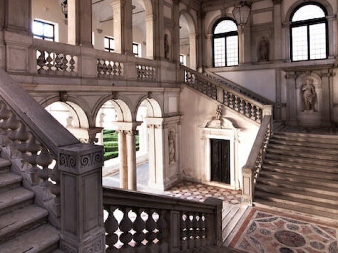Украшенный интерьер с арочными дверными проемами, мраморными колоннами и парадной лестницей, ведущей на верхний уровень с большими окнами.