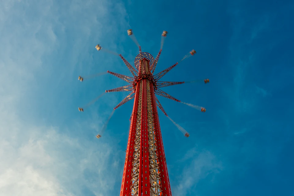 A tall red amusement ride with spinning swings against a clear blue sky.