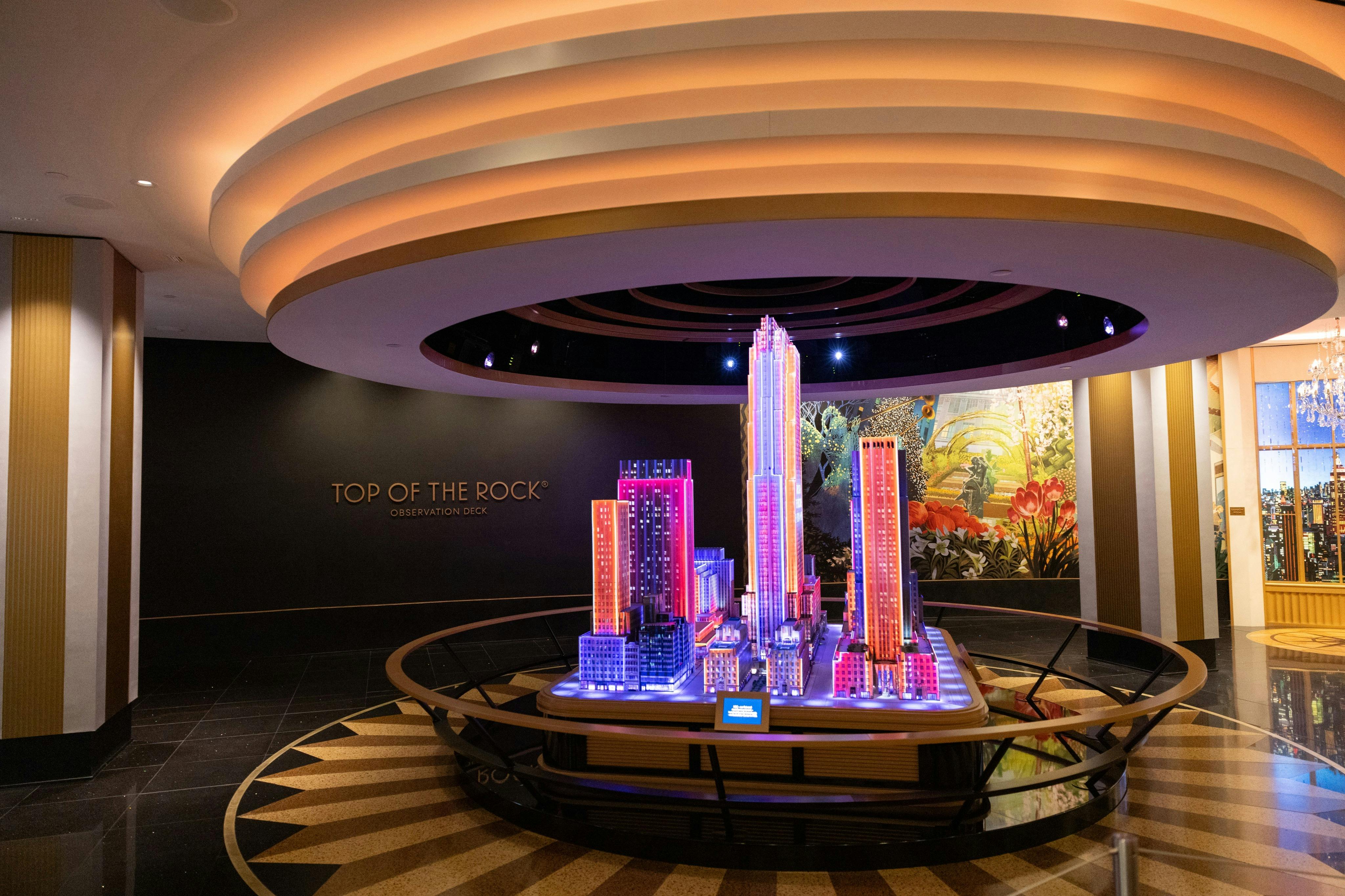 A lit-up scale model of New York City skyscrapers at the Top of the Rock Observation Deck, surrounded by modern decor.