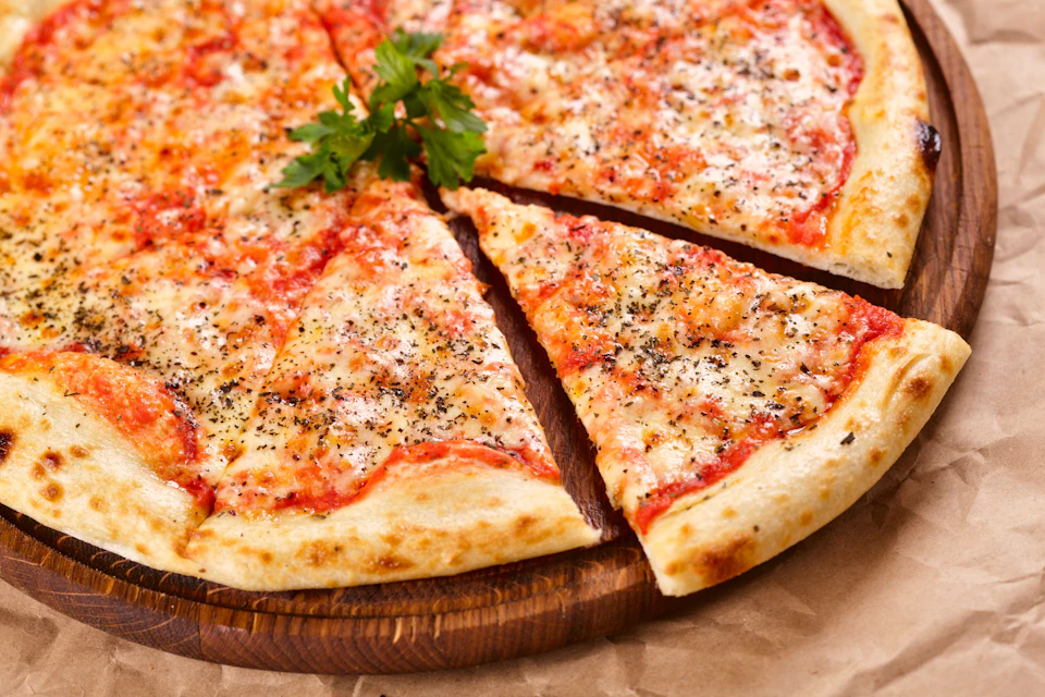 Pepperoni pizza with a garnish of parsley on top, displayed on a wooden board. A slice is slightly pulled away.