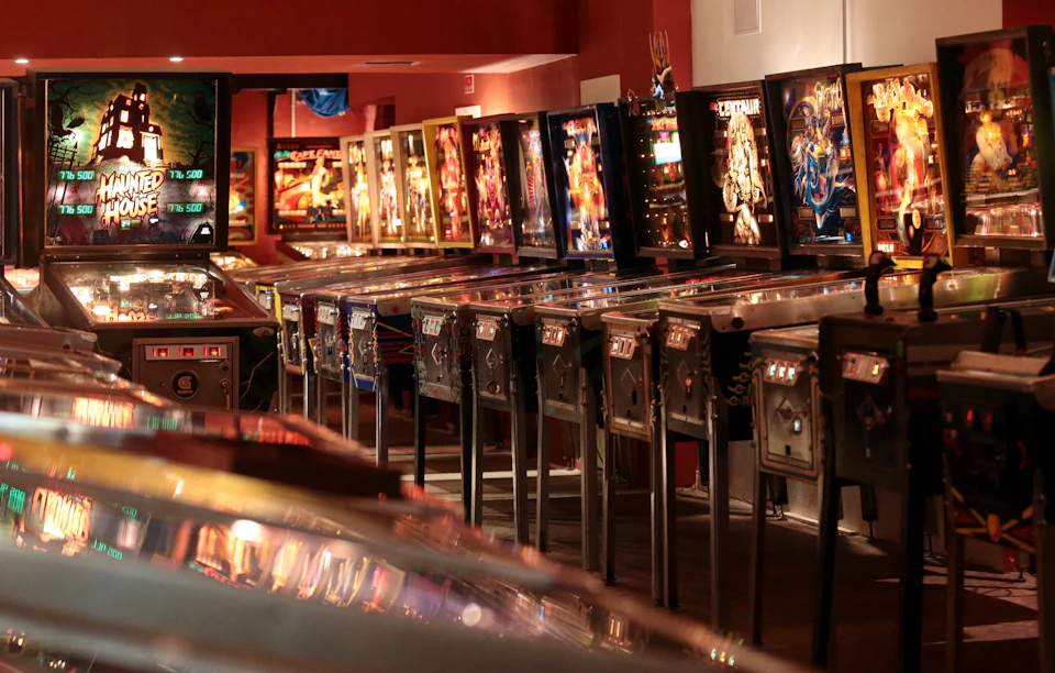A row of pinball machines in a dimly lit arcade with colorful, illuminated backboards.