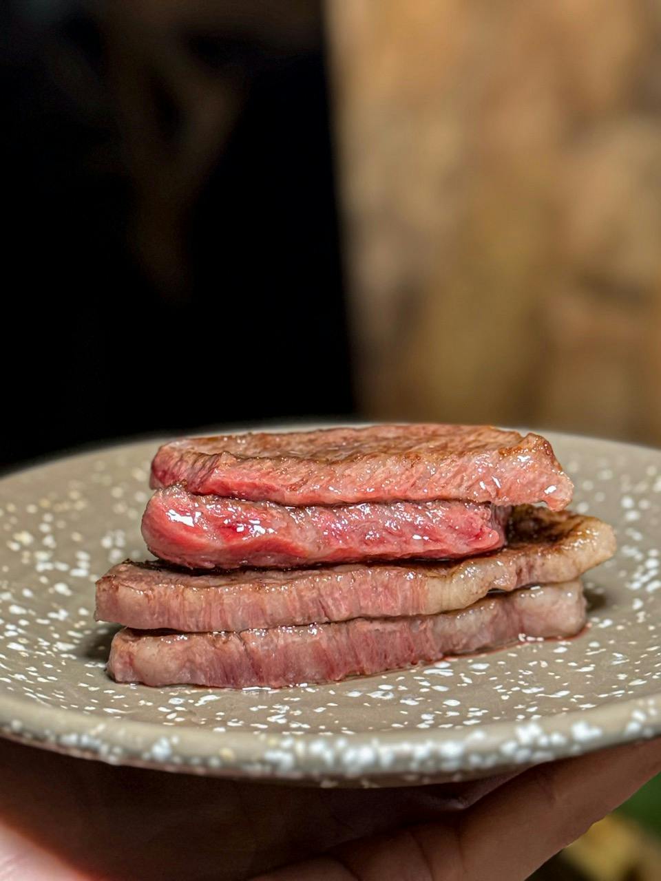 Three slices of cooked steak stacked on a speckled ceramic plate.