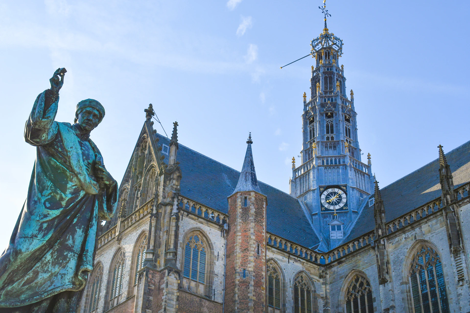 A historic church with a tall clock tower and a statue in the foreground under a clear blue sky.