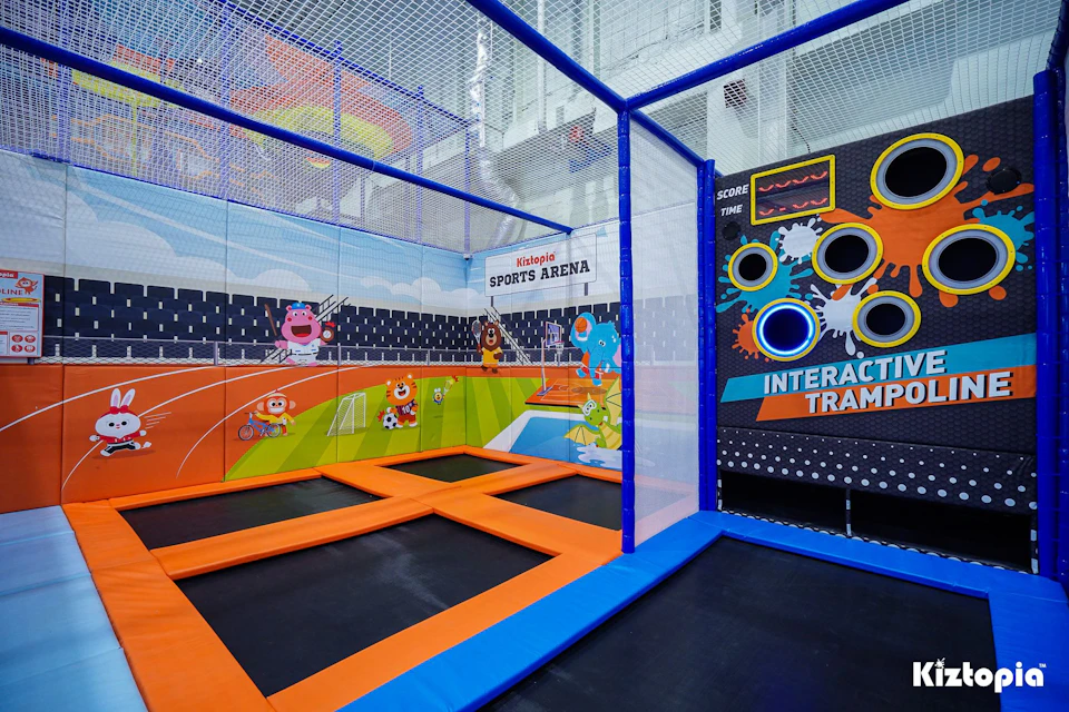 A colorful indoor trampoline area with sports-themed decorations and interactive games on the wall.