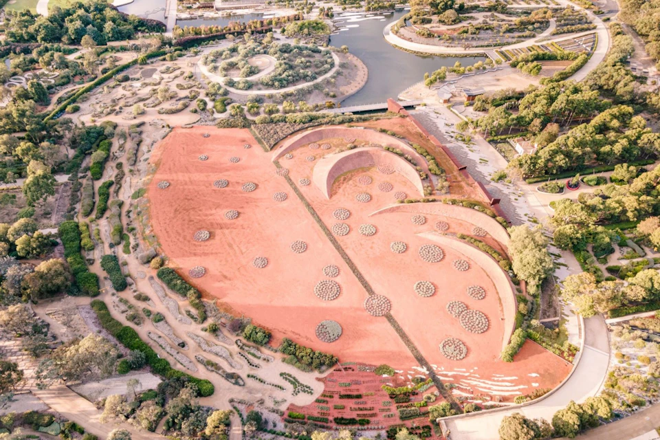 Aerial view of a desert garden with circular plant clusters, winding pathways, and a large spiraling structure.