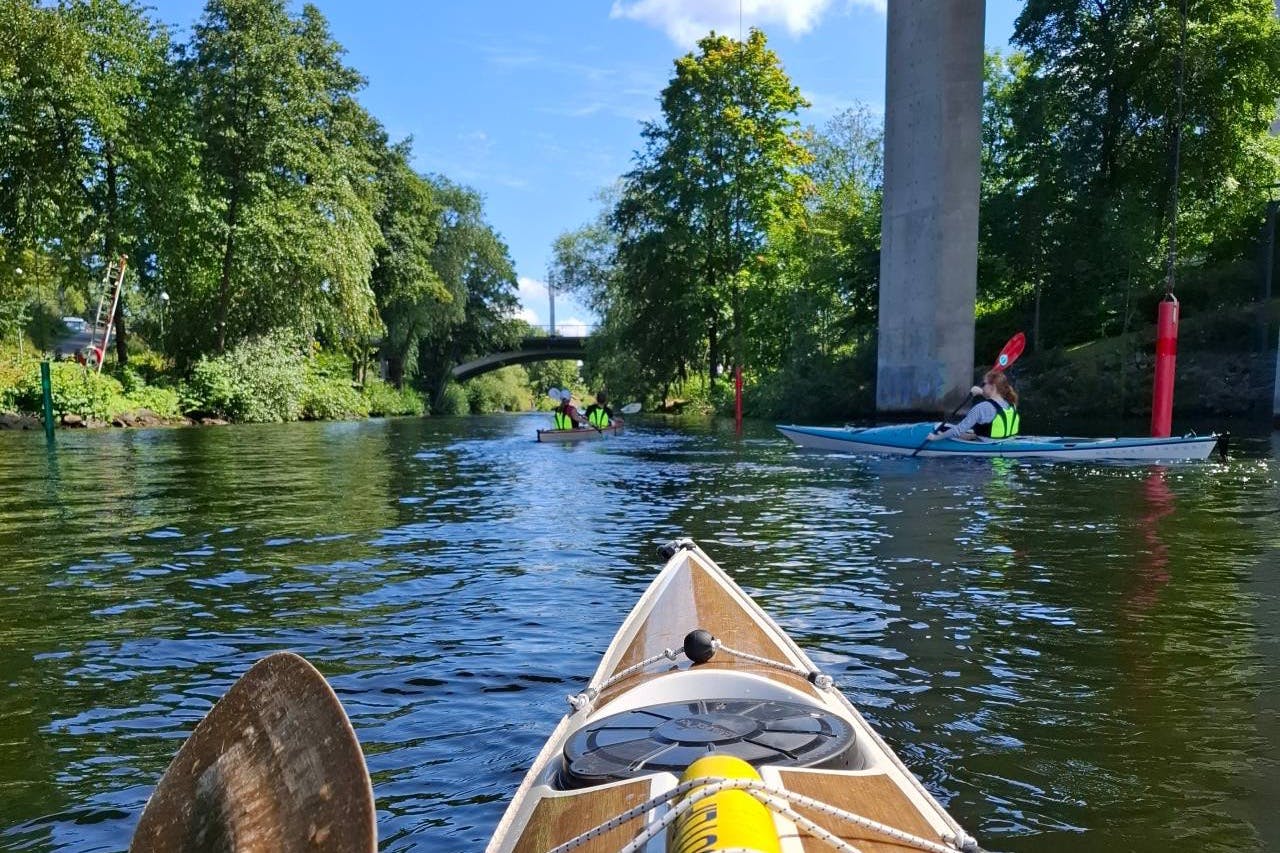 Kayakistes pagayant sur une rivière entourée d'arbres, avec un pont et un pilier en béton à l'arrière-plan.