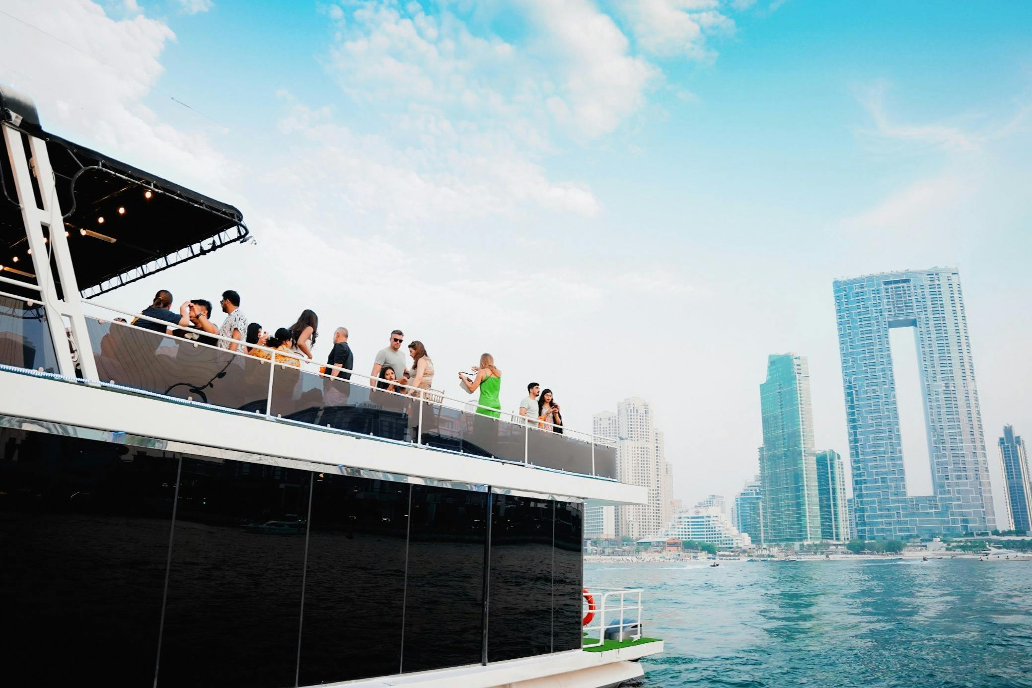 Люди общаются на верхней палубе лодки с городскими небоскребами и голубым небом на заднем плане.