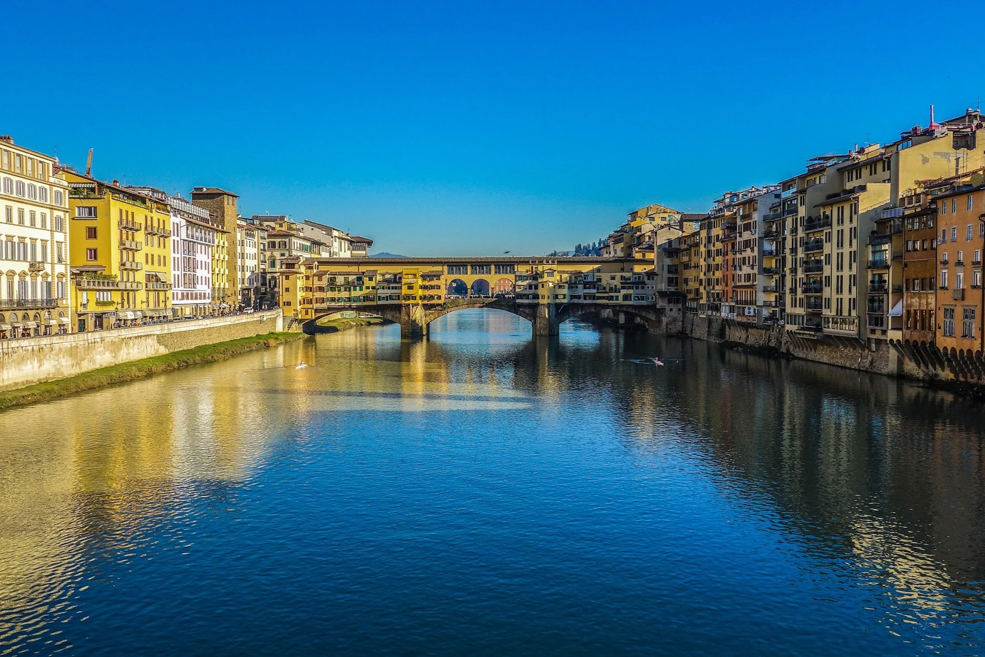 A historic bridge over a calm river with buildings on both sides under a clear blue sky.