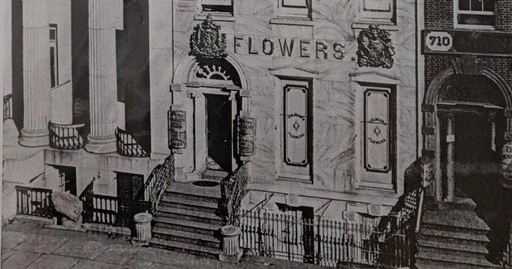 A historical building facade with a sign reading 'Flowers,' decorative details, and a staircase leading to the entrance.
