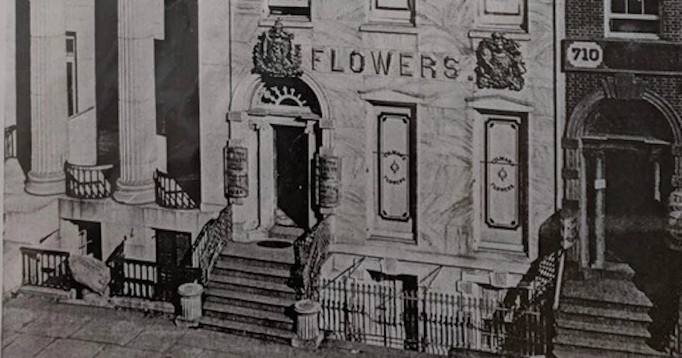 A historical building facade with a sign reading 'Flowers,' decorative details, and a staircase leading to the entrance.