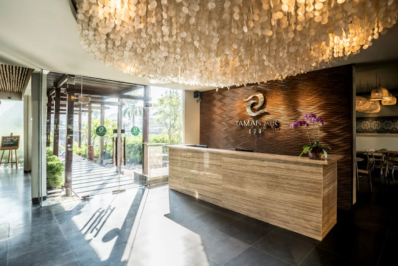 A modern spa reception area with a wood-textured wall, a decorative ceiling, a stone desk, and glass entrance doors.
