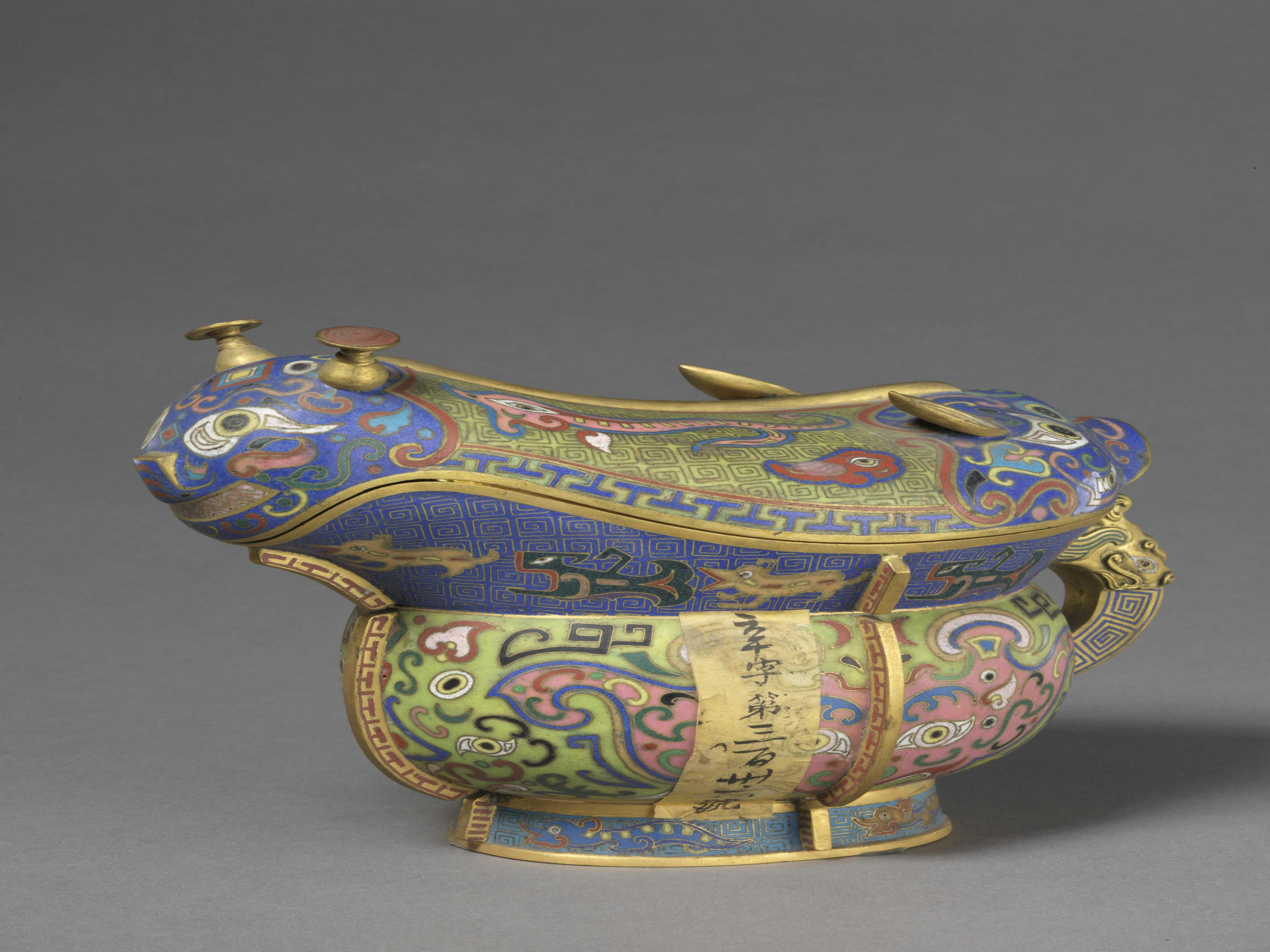 An ornate, colorful cloisonné vessel in the shape of an animal, decorated with intricate patterns and calligraphy.
