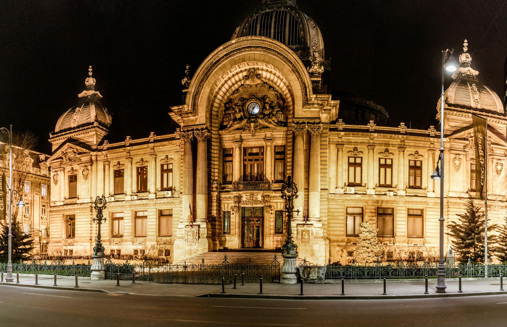 Illuminated grand building with ornate architecture and a central clock, viewed at night with a clear, dark sky.