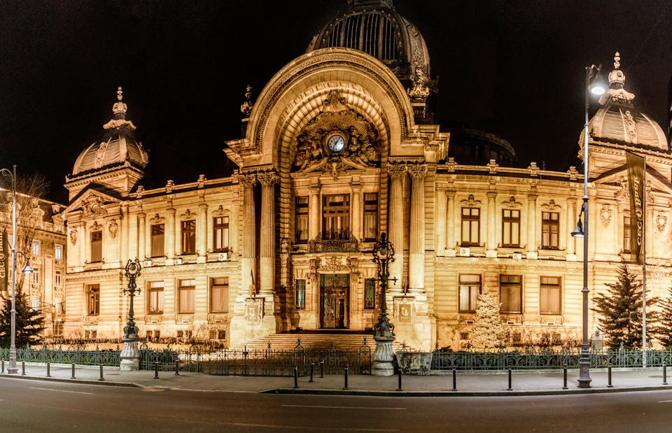 Illuminated grand building with ornate architecture and a central clock, viewed at night with a clear, dark sky.
