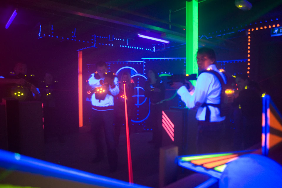 People wearing illuminated vests and holding laser guns in a dark, neon-lit laser tag arena.