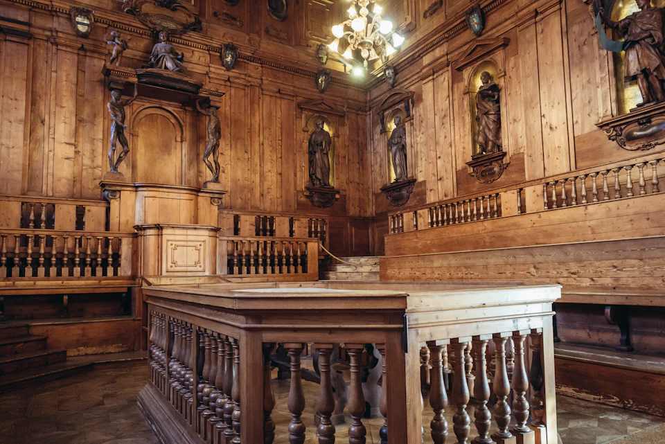 A historic wooden courtroom with statues, paneling, railings, and a chandelier. No people are present.