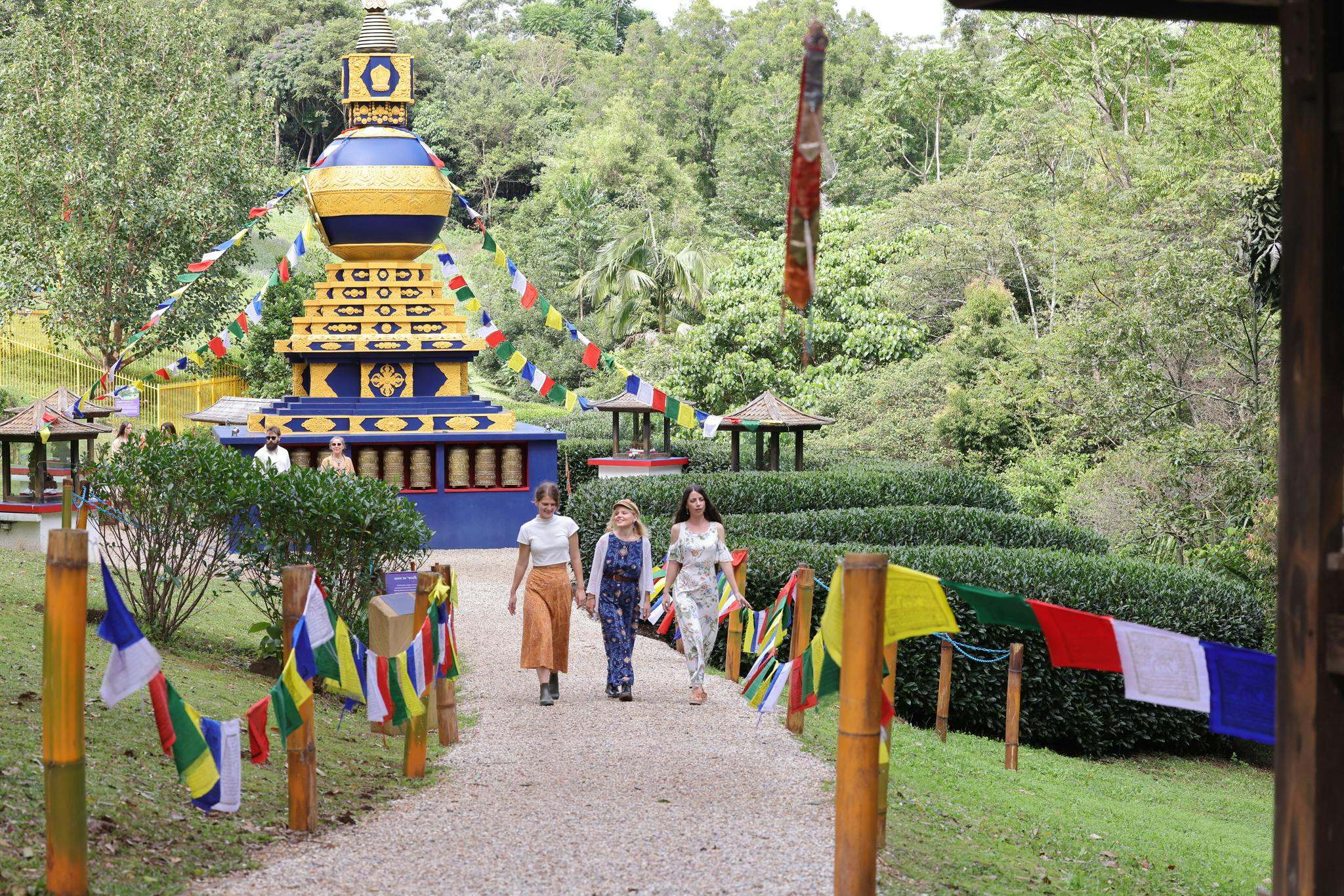 色とりどりの祈りの旗で飾られた道を歩く3人の人が、緑豊かな環境の中で活気に満ちた仏塔に通じています。